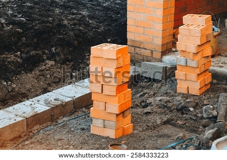 Construction site featuring red bricks stacked upright on freshly dug ground with foundation work underway