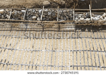 Construction site featuring slope stabilization with rock gabion basket and steel rebar reinforcement grid on ground prepared for concrete work displaying industrial structure process