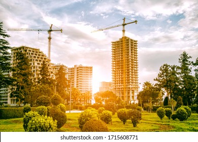 Construction Site With Green Park Area. Cranes And Buildings In Morning Sun