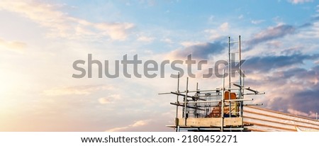Construction site with a house being built from brick and timber, featuring brickwork, roof trusses and scaffolding. House roof construction in progress. Space for text. Banner concept