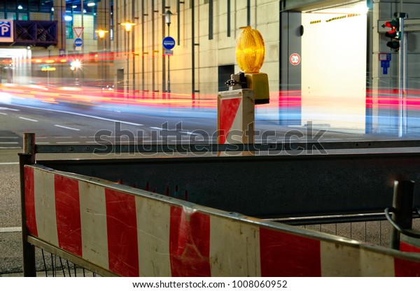 Construction site lamp at a construction\
site at night with flowing traffic in the\
background