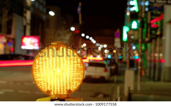 Construction site lamp at a construction\
site at night with flowing traffic in the\
background