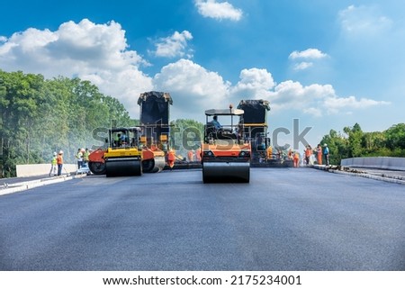 Construction site is laying new asphalt pavement, road construction workers and road construction machinery scene. Highway construction site scene.