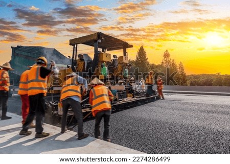 Construction site is laying new asphalt pavement, road construction workers and road construction machinery scene. Highway construction site scene.