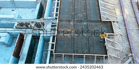 A construction site with a man in a yellow hard hat working on a project. Concept of hard work and progress, as the man is seen laying down wooden boards and working on a concrete slab