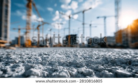 A construction site with multiple cranes and buildings under construction, with a close-up view of gravel in the foreground.