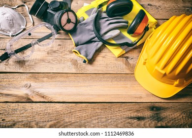 Construction site safety. Protective hard hat, headphones, gloves, glasses and masks on wooden background, copy space, top view - Shutterstock ID 1112469836