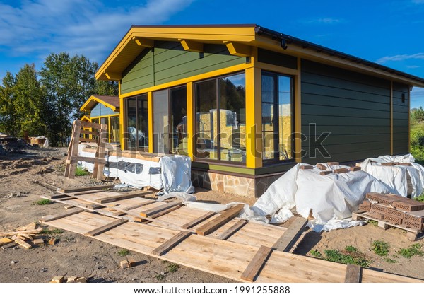 Construction site for suburban house. Construction\
site near wooden cottage. Erection scandinavian-style dwelling\
cottage. Newly built house near uncleaned construction site.\
Erection country\
houses