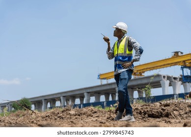 Construction site supervisor using walkie talkie at infrastructure project, Portrait of a civil engineer with radio communication at a bridge construction and railway project