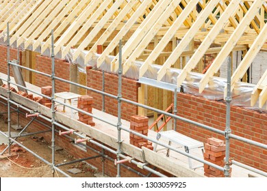 Construction site in UK with a house built from brick and timber, featuring brickwork, roof trusses and scaffolding - Shutterstock ID 1303059925