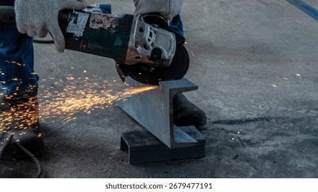 At a construction site, a worker uses an angle grinder to cut a steel beam, creating sparks that fly into the air. The scene shows the focus and effort involved in metalwork
