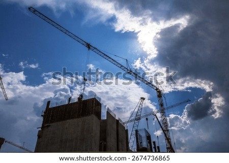 Construction site with workers and tower cranes against dramatic cloudy sky. Industrial background of construction process, urban development and architecture.