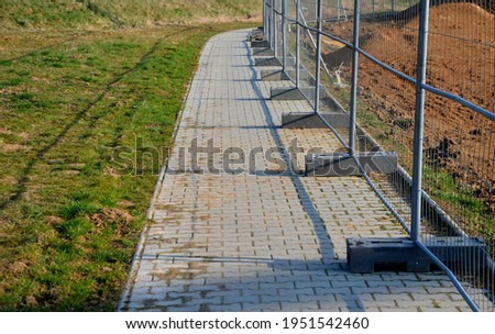 Construction sites with portable fence parts that are installed in plastic weight racks hold the stability of the fencing. along the sidewalk made of interlocking paving