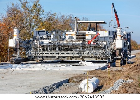 Construction of a solid reinforced road, a high performance concrete paver at the construction of a new highway on a bright autumn day.