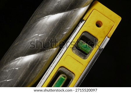 Construction spirit level aligned vertically next to metal surface on black background.