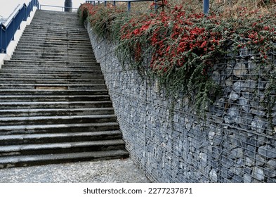 construction of a steep staircase by the stone wall car park with high durability even under heavy load galvanized steel floor grate and railings. gabion above him a wire fence. corridor, narrow - Shutterstock ID 2277237871