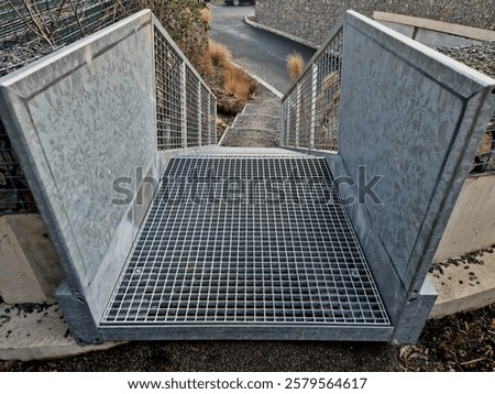 construction of a steep staircase by stone wall car park with high durability even under heavy load galvanized steel floor grate and railings. gabion above him wire fence. corridor, flowerbed
