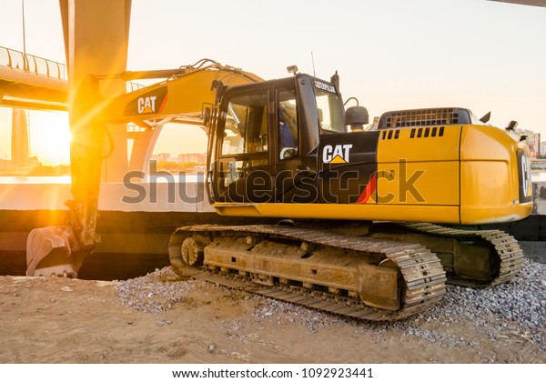 Construction of street of new\
emankment at St. Petersburg, Russia. Excavator CAT Caterpillar.\
Tractor with sunset shines. earthmoving, transportation.\
construction\
machinery\
concept.