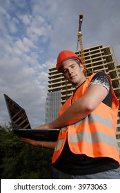 Construction Supervisor In Safety Helmet And Reflex Vest With Notebook In Front Of Construction Site.