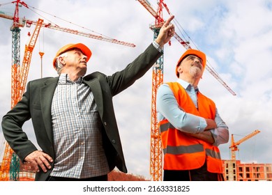 Construction supervisor, workers at a construction site. Managers wearing protective workwear, hard hat looking up pointing, construction cranes on skyline. Construction workforce, working labor man.