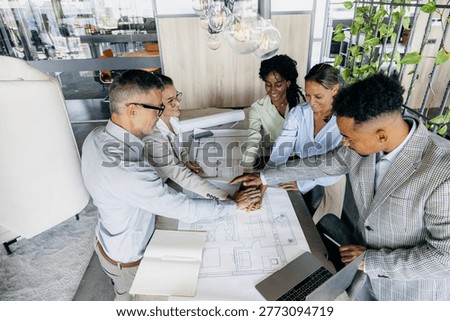 Construction supervisors coordinating kickoff plans over blueprint, diverse