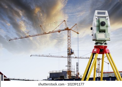 construction surveying instrument, large building industry in background, sunset