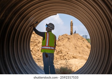 Construction surveyor or engineer working in pipe construction site with torch for inspection detail of construction with heavy machinery excavator constructed hi-way road background.