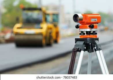 Construction Surveyor Equipment Theodolite Level Tool During Asphalt Paving Works With Compactor Roller At Background