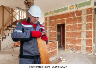 Construction Team Leader. Man Measures Boards With Ruler. Guy Measures Parquet Board. Foreman In Construction Uniform. Foreman Stands In Unfinished Building. Man Foreman In Workplace