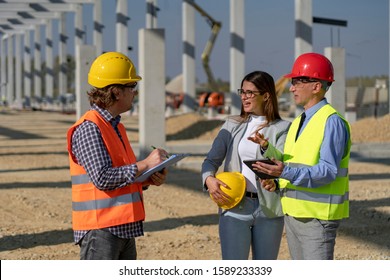 Construction Team Standing And Talking On Site Under Construction. Business, Building, Teamwork And People Concept. Project Management And Field Crew Meeting On Construction Site.