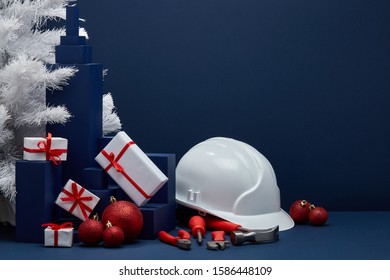 Construction tools, hard hat, white fir tree, gift boxes and Christmas ornaments on dark blue background with copy space. New Year and Christmas construction background. For advertising or web design - Powered by Shutterstock