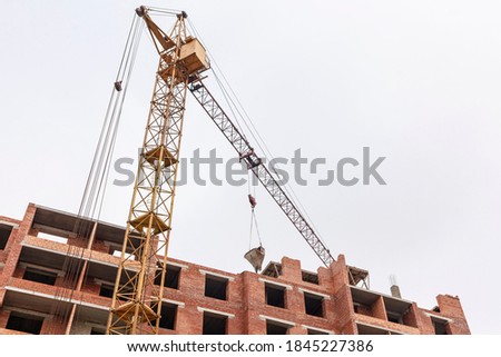 Construction tower crane on a background of sky and brick house. The tower crane on the construction site feeds the mortar upwards