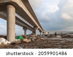 Construction of an urban multi-level road junction. Concrete overpass on high supports. The process of building roads and bridges. Building materials, debris and dirt. Bottom view