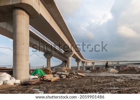 Construction of an urban multi-level road junction. Concrete overpass on high supports. The process of building roads and bridges. Building materials, debris and dirt. Bottom view