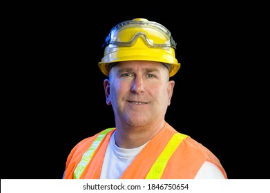 A Construction Utility Worker Wearing Protective Safety Equipment Including A Hard Hat, Safety Goggles And A Reflective Orange Vest Smiles Against A Black Background.