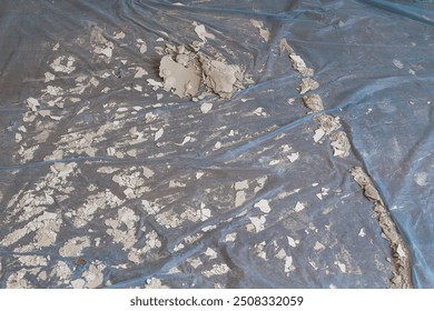 Construction waste. Dried and peeling paint plates; plaster and concrete waste. Nylon cleaning tarpaulin spread on the ground. - Powered by Shutterstock