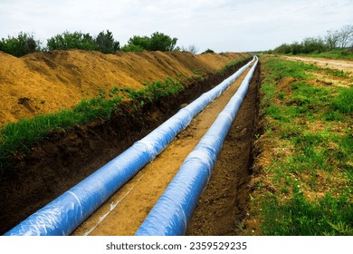 Construction of a water conduct. Double thread of large diameter water pipe is laid through plain fields, arid terrain. Pipe was laid in earthen trench and wrapped with plastic wrap prevent corrosion