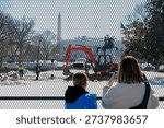 Construction work is in progress at the White House in the winter with people observing and taking pictures from behind a fence