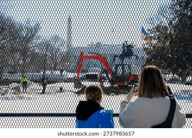 Construction work is in progress at the White House in the winter with people observing and taking pictures from behind a fence