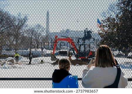 Construction work is in progress at the White House in the winter with people observing and taking pictures from behind a fence