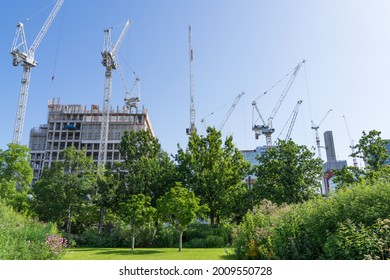 Construction work taking place in the Queen Elizabeth Olympic Park in Stratford on a sunny day. Cranes and under construction building sticking up above the trees. London - 17th July 2021