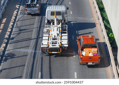 Construction work is underway on a bustling city street as a large truck and an orange delivery vehicle navigate their way past roadwork.