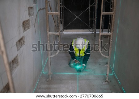 A construction worker accurately measures with a laser level in an industrial setting ensuring precise alignment.