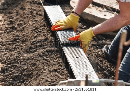 Construction worker actively installing plastic channel drainage system for future parking bay, using  hammer and  tools to adjust components