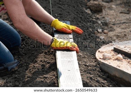 Construction worker actively installing plastic channel drainage system for future parking bay, using  hammer and  tools to adjust components