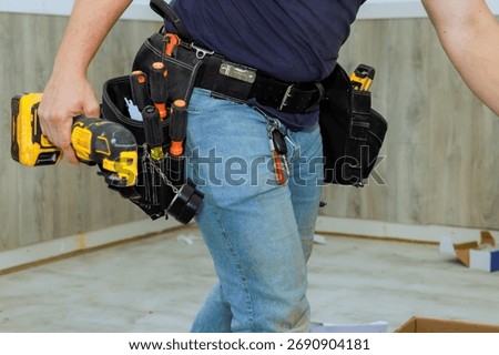 Construction worker is actively using power drill in home under renovation, using tool belt equipment.