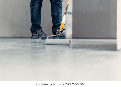 A construction worker apply grey epoxy resin in an industrial hall