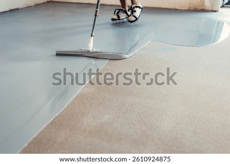 Construction worker applying epoxy resin on concrete floor using a trowel
