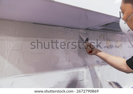 Construction worker applying joint compound to kitchen wall with a putty knife, prepping surface for tile installation during renovation