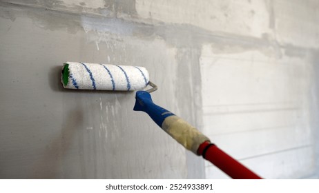 Construction worker is applying plaster on a grey wall using a roller, during renovation works.